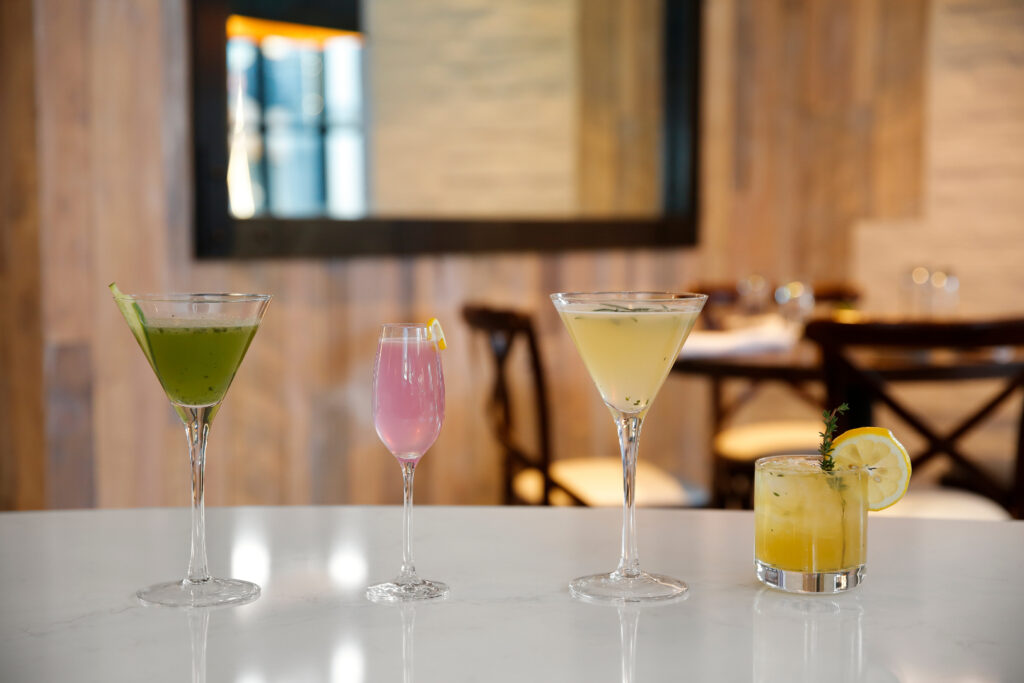 Green, pink, tan, and yellow cocktails lined up on top of a white bar top