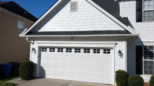 Traditional white double garage door with raised panels and a top row of grid windows on a white siding home.