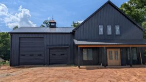 Modern black metal barn featuring a high-clearance RV garage door and a standard black sectional garage door.