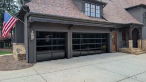 One single and one double modern black-framed glass garage doors with tinted privacy panels on a dark grey luxury home.