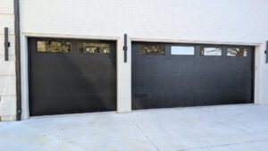 Sleek matte black modern garage doors with a single row of tinted rectangular windows on a white brick house.