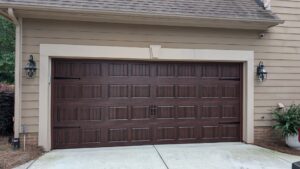 Luxury dark wood-grain carriage house garage door with vertical panels and decorative black handles on a beige home.