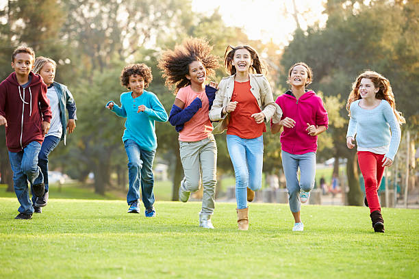 a Group Of Young Children Running Towards Camera In Park Smiling