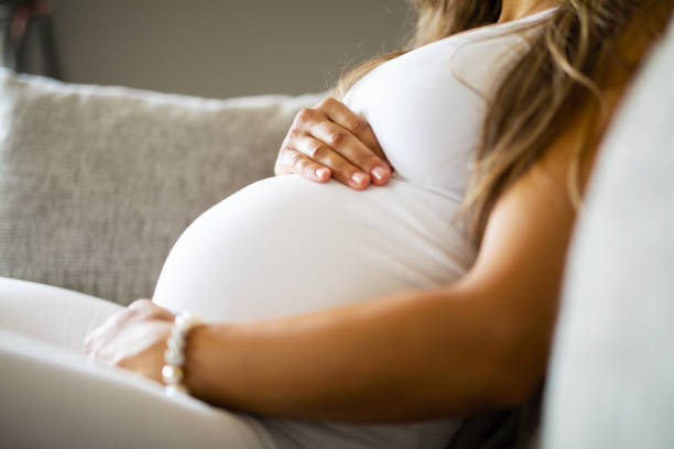 a pregnant women in white shirt and white pants sitting comfortably on a couch