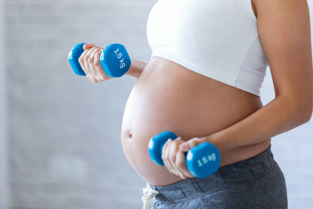 a pregnant woman exercising lifting weights, dispelling one of the most common pregnancy myths: that pregnant women shouldn't or can't exercise.