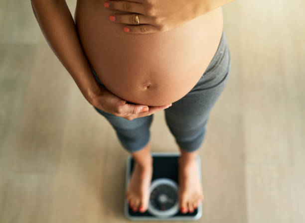 a pregnant woman standing on a scale measuring her weight.