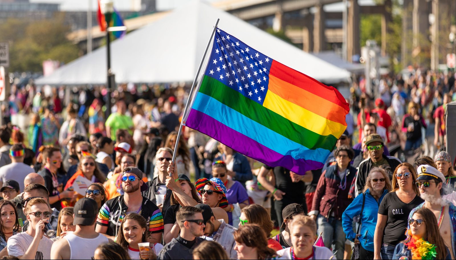 a crowd holding a rainbow flag in support of LGBTQIA+ Pride